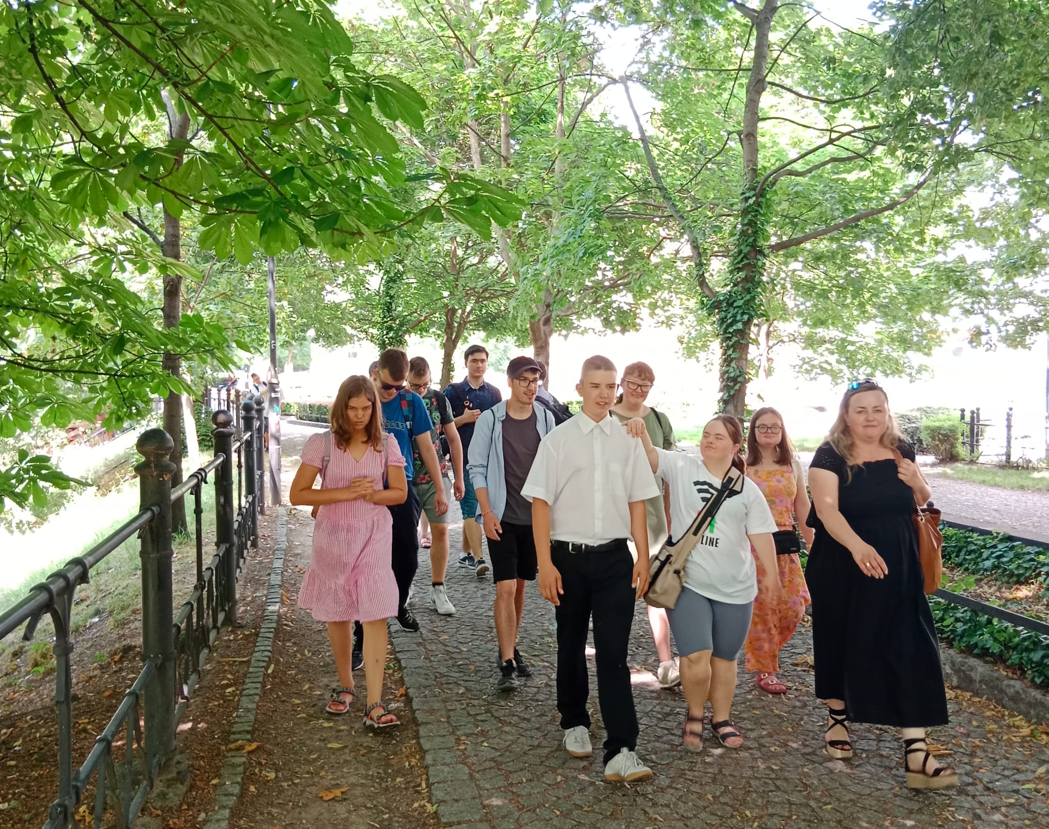 Na zdjęciu widzimy młodzież idącą w kierunku Hotelu Monopol. Trasa w cieniu drzew prowadzi wzdłuż fosy miejskiej przy ulicy Podwale we Wrocławiu.