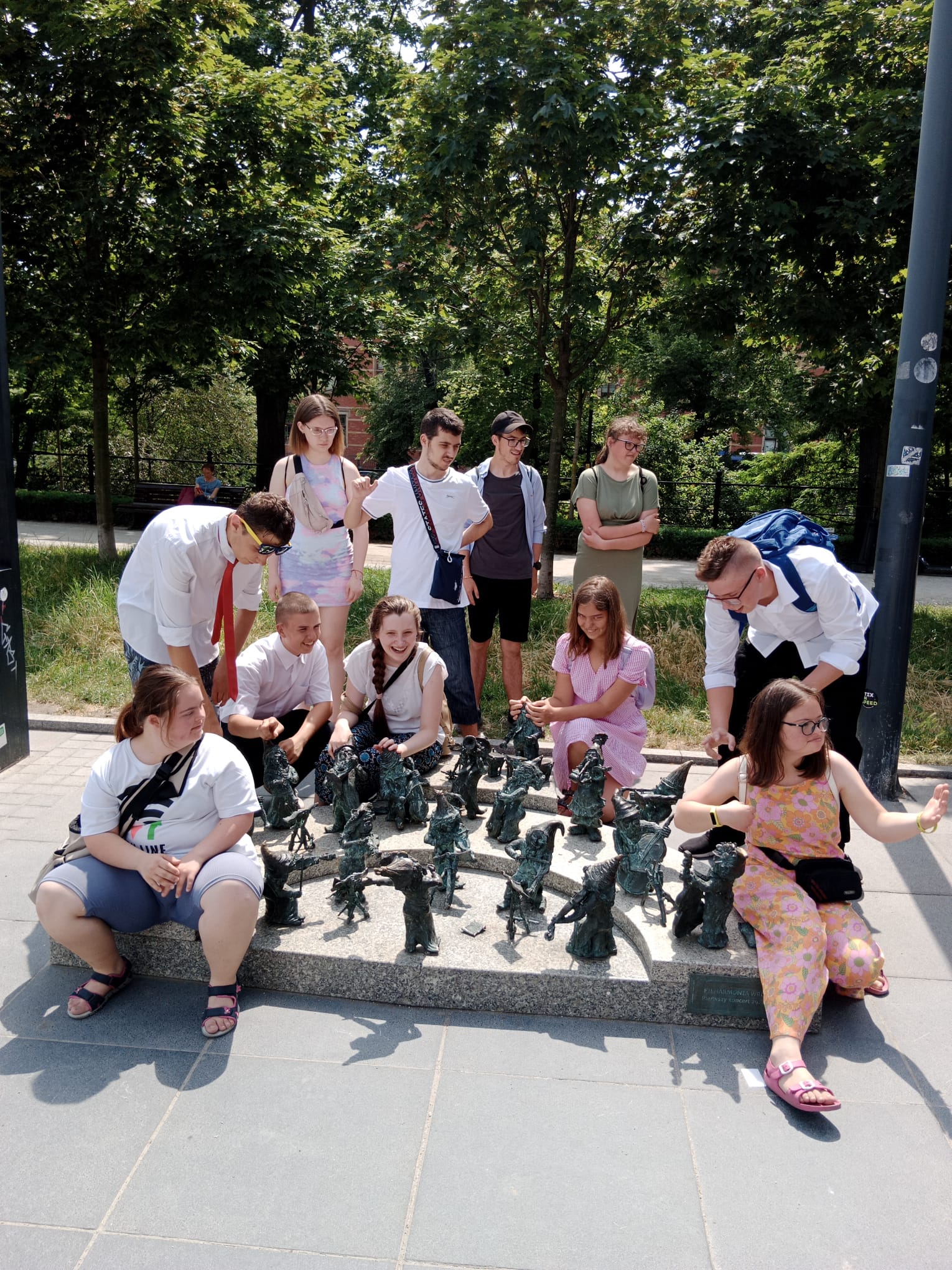 Młodzież zatrzymała się na Placu Wolności przy rzeźbie krasnali wrocławskich. Są to Krasnale Muzycy. Uczniowie na zdjęciu naśladują orkiestrę.